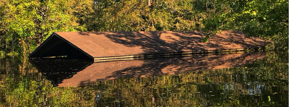 Flooding at Moores Creek on September 17, 2018 A pitched roof can be seen just above water with trees surrounding.