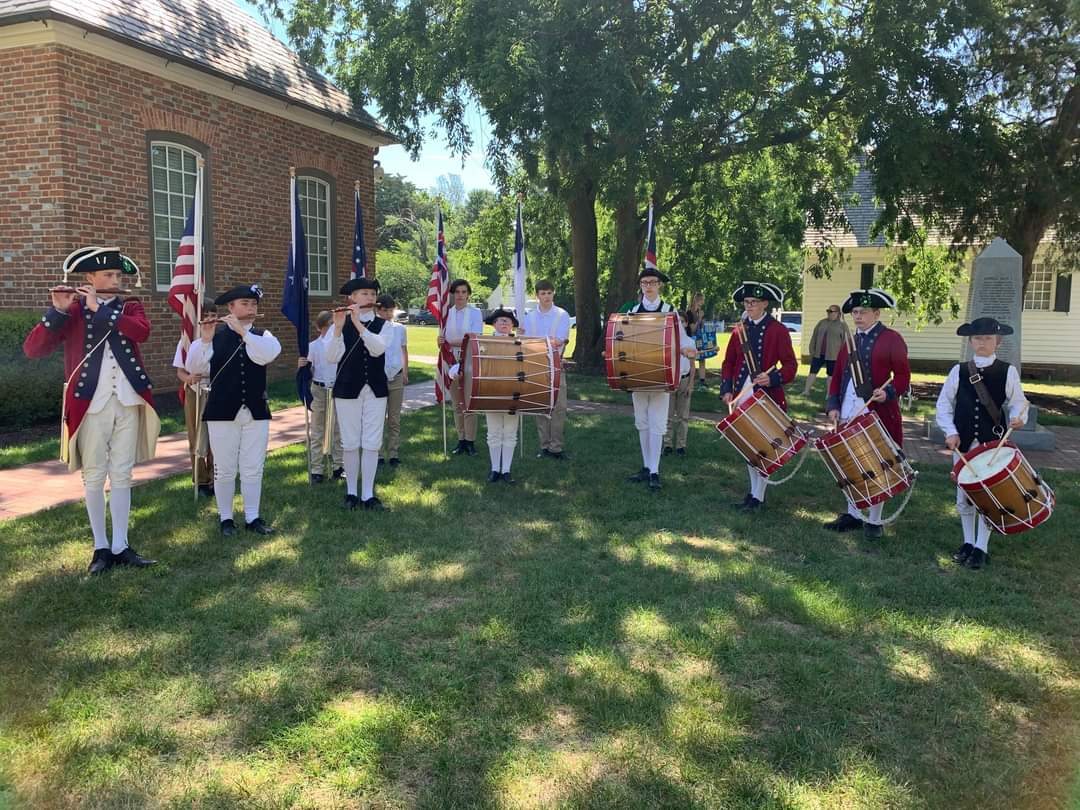Fifes and Drums of Yorktown New Group of young colonial musicians holding instruments standing in front of a brick building.