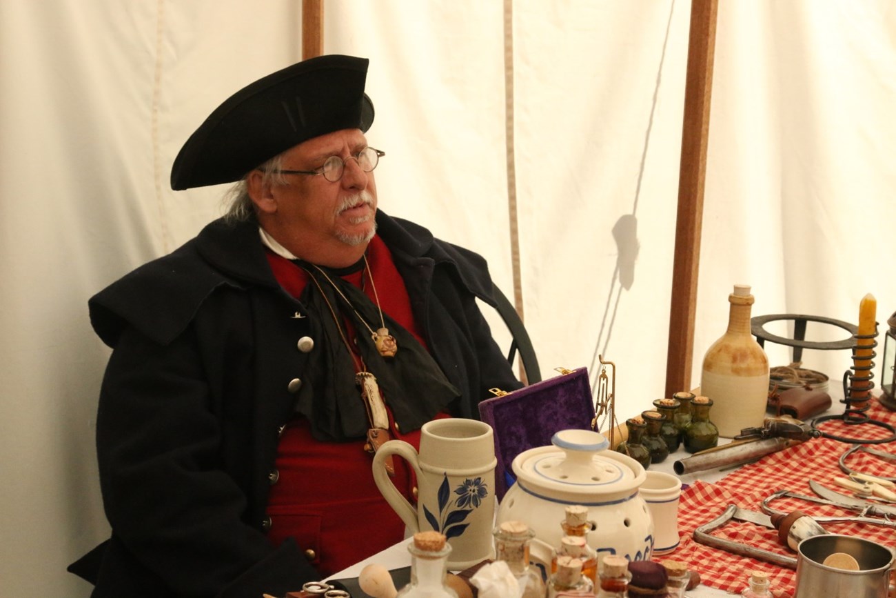 Colonial doctor sit's in front of medicine table