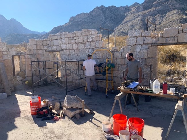 Volunteers work on restoring a rock wall on an old cabin site with a tall mountain in the background