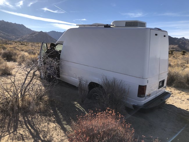 A white van with its tires buried deep in the sand.