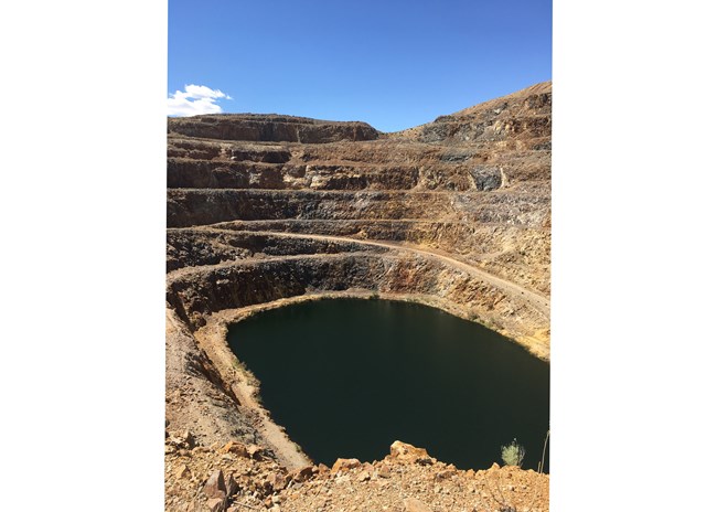 A giant water-filled pit with a road leading around the pit towards the water