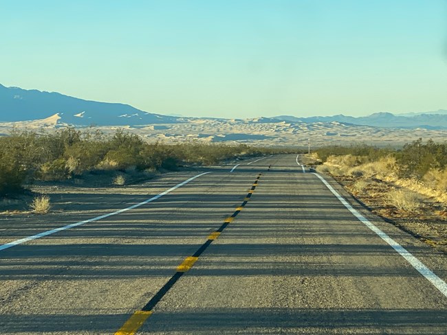 A paved desert road with dunes in the background