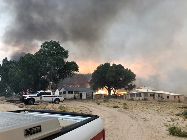 A residence and various outbuildings at Kessler Springs Ranch, with flames creeping up behind them.