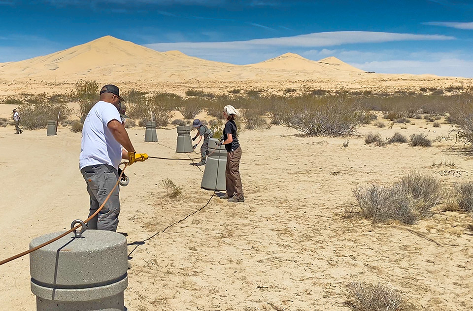 volunteers threading cable volunteers thread steel cable through eyelets in concrete bollards with dunes in background