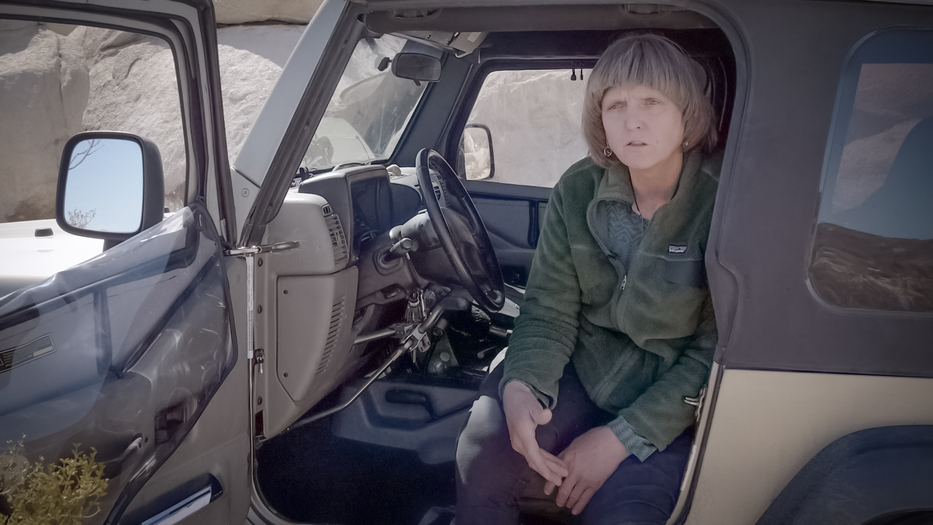 Debra Hughson Explaining Cima Dome Ecology A women sits in a four-wheel-drive vehicle with the door open and facing the camera while in the middle of explaining the ecosystem of Cima Dome