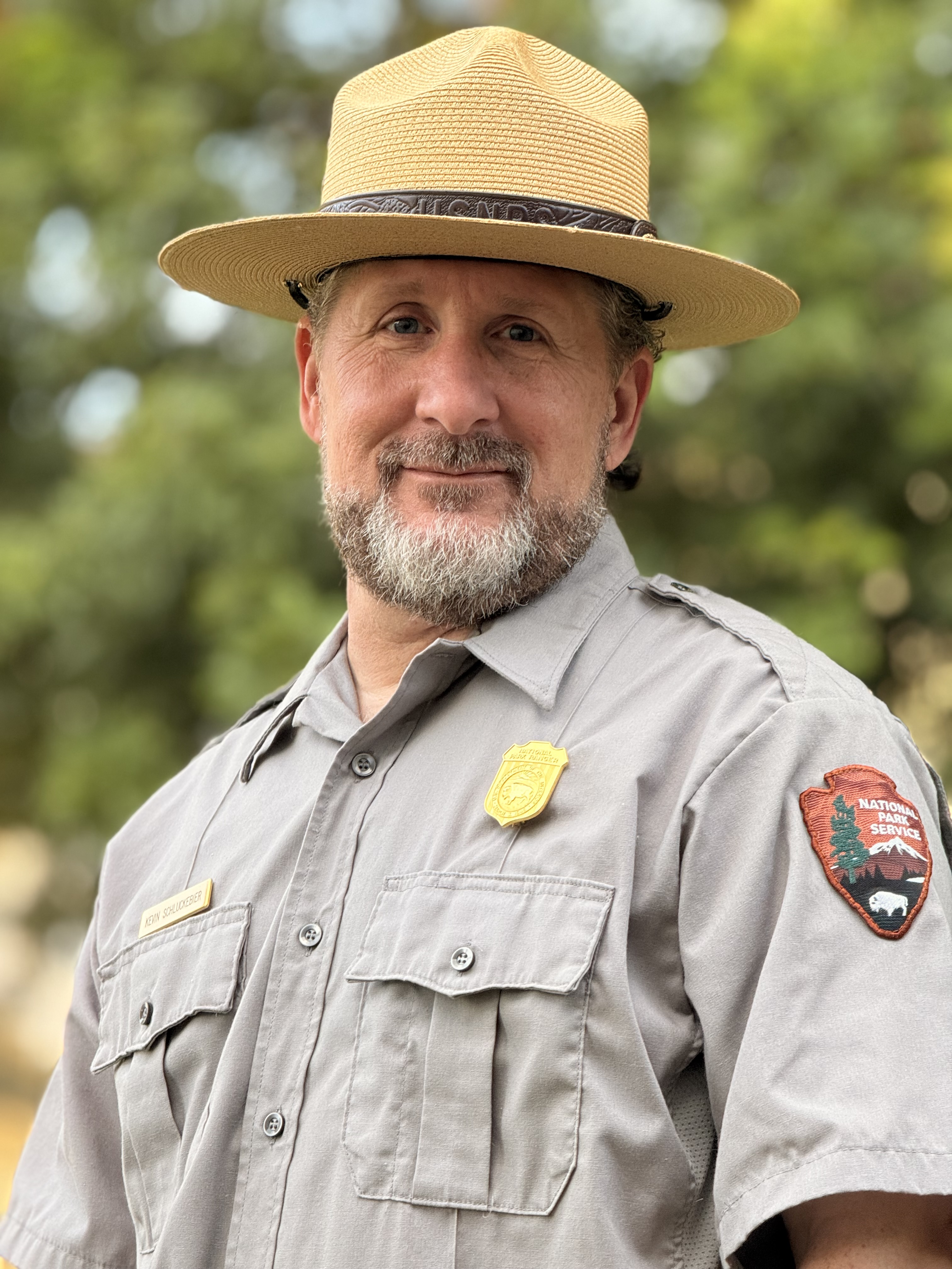 a man in a grey uniform shirt and a straw flat brimmed hat