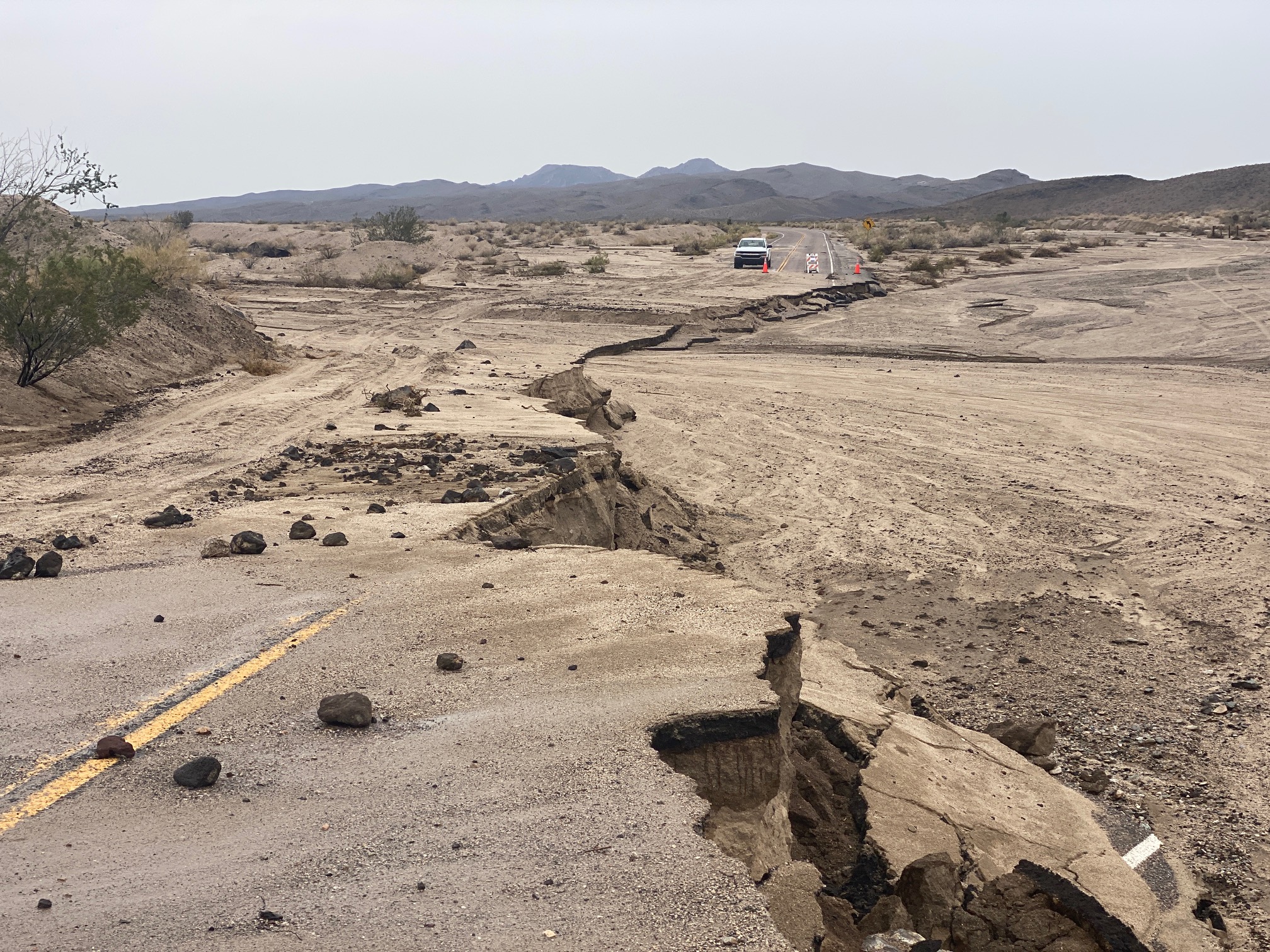 A paved road with debris on it abruptly ends, dropping off into a washed out section of dirt and debris