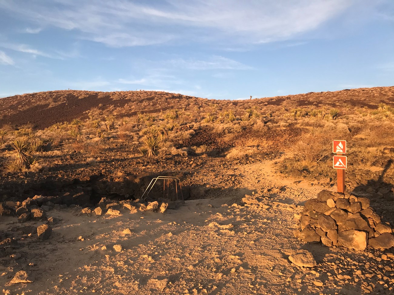 Lava Tube Entrance. Metal stairs lead underground. Lava and creosote surround the stairs.