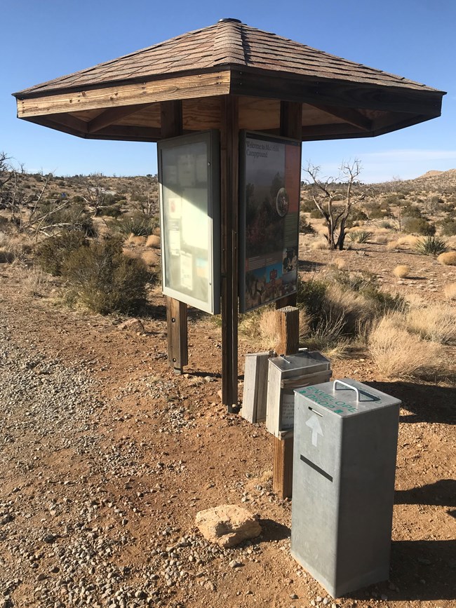 A triangle information board; a pole with plastic boxes for camping registration; iron fee box.