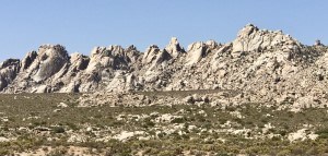 The rocky slopes of the Granite Mountains seen from the Boulders Viewpoint.  Creosote and large rocks in the foreground.