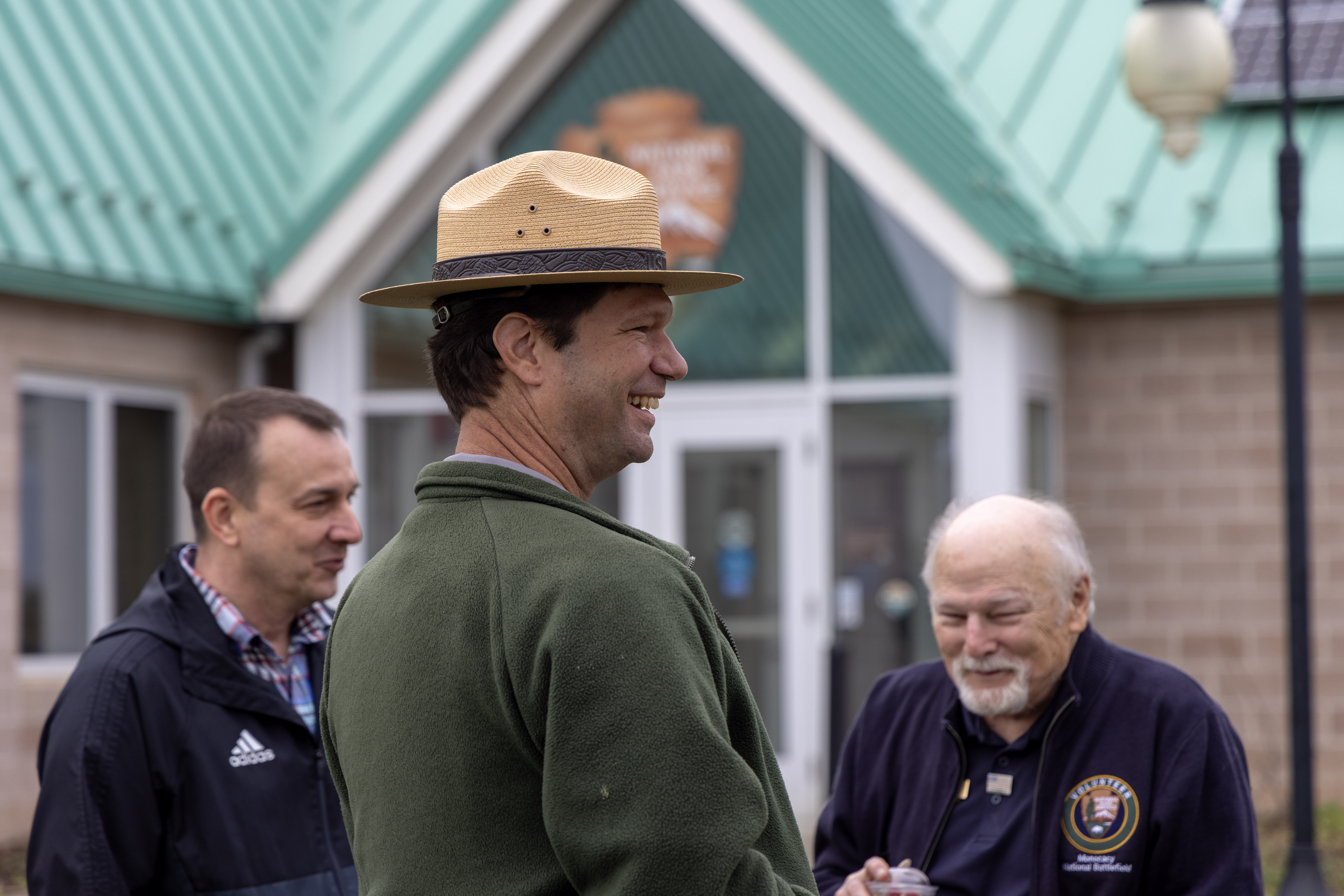 A ranger smiles while talking to a visitor and volunteer outside the visitor center.