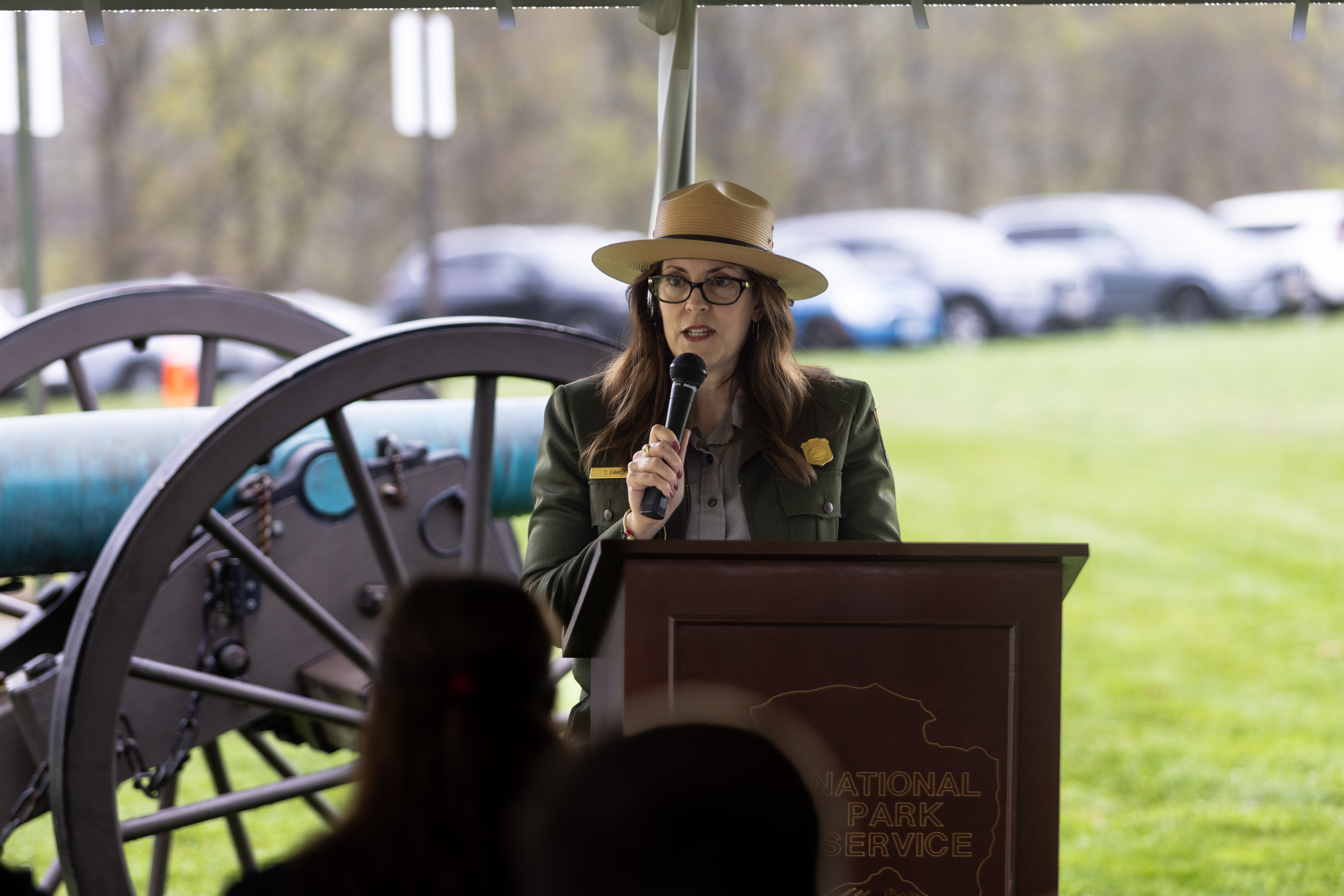 Park chief of resource, education and visitor services standing behind a podium and speaking to an outdoor crowd.