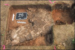 The corner of a stone foundation is revealed beneath the surface in a square hole.