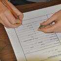 A worker writes on a form while holding an artifact in their other hand