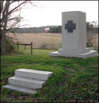 White stone monument with bronze Greek cross on front.