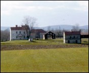 Green farm fields with a two-story white building in the background.