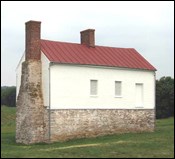 A small two-story building with stone walls on first floor and white on the second story.