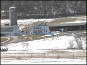 A farm with snow on the ground. A farm house and barn in the background.