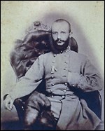 Middle-aged man seated in an elaborate chair with left hand tucked into the breast of his Confederate uniform.