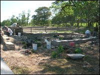 Stone masons apply mortar and relay stones in the foundation of the blacksmith shop.