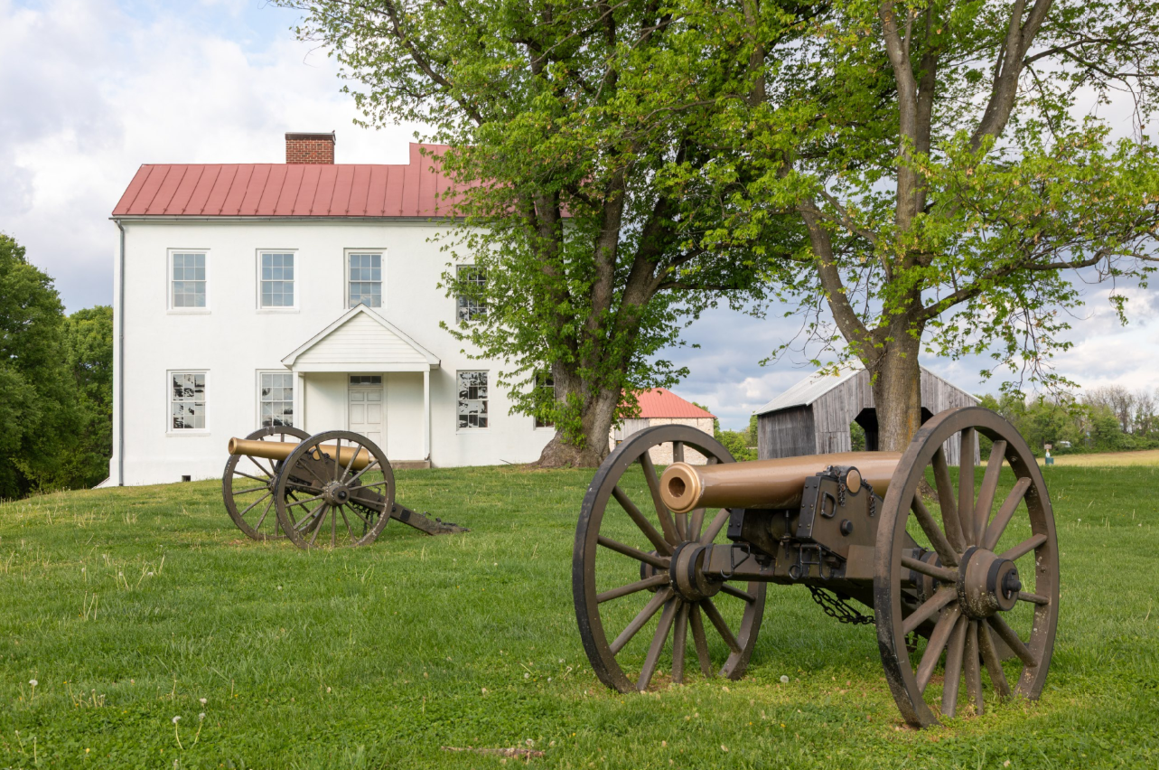 Two Civil War-era cannons sit on a grassy field at Monocacy National Battlefield, with a white farmhouse in the background.