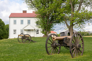 Two Civil War-era cannons sit on a grassy field at Monocacy National Battlefield, with a white farmhouse in the background.