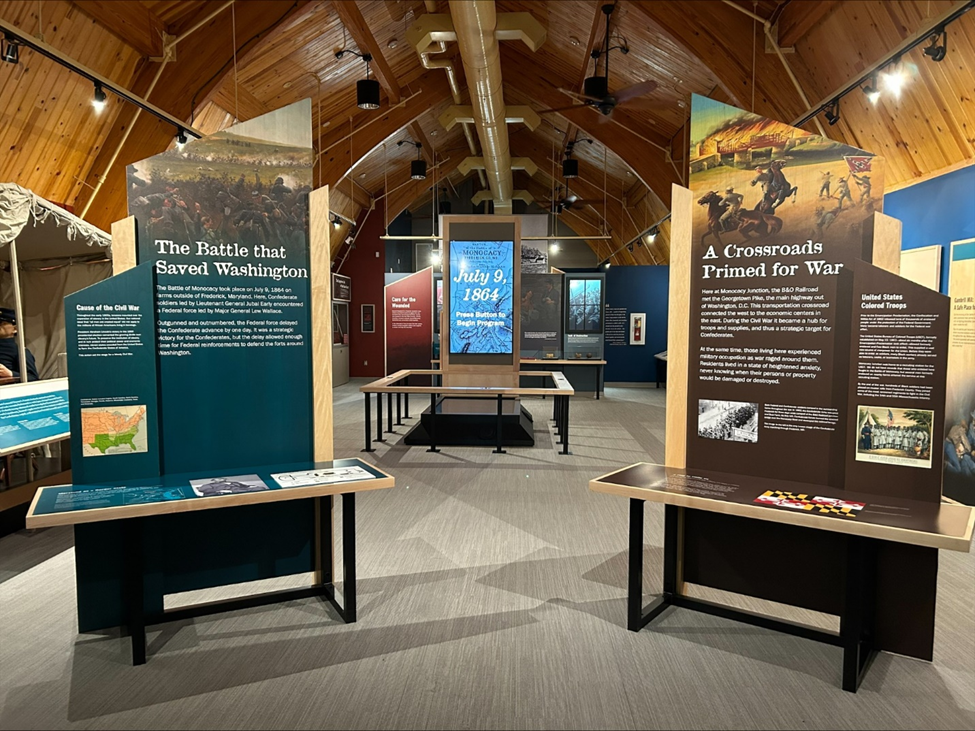 Several colorful displays about a Civil War battle are arrayed under a barn roof.