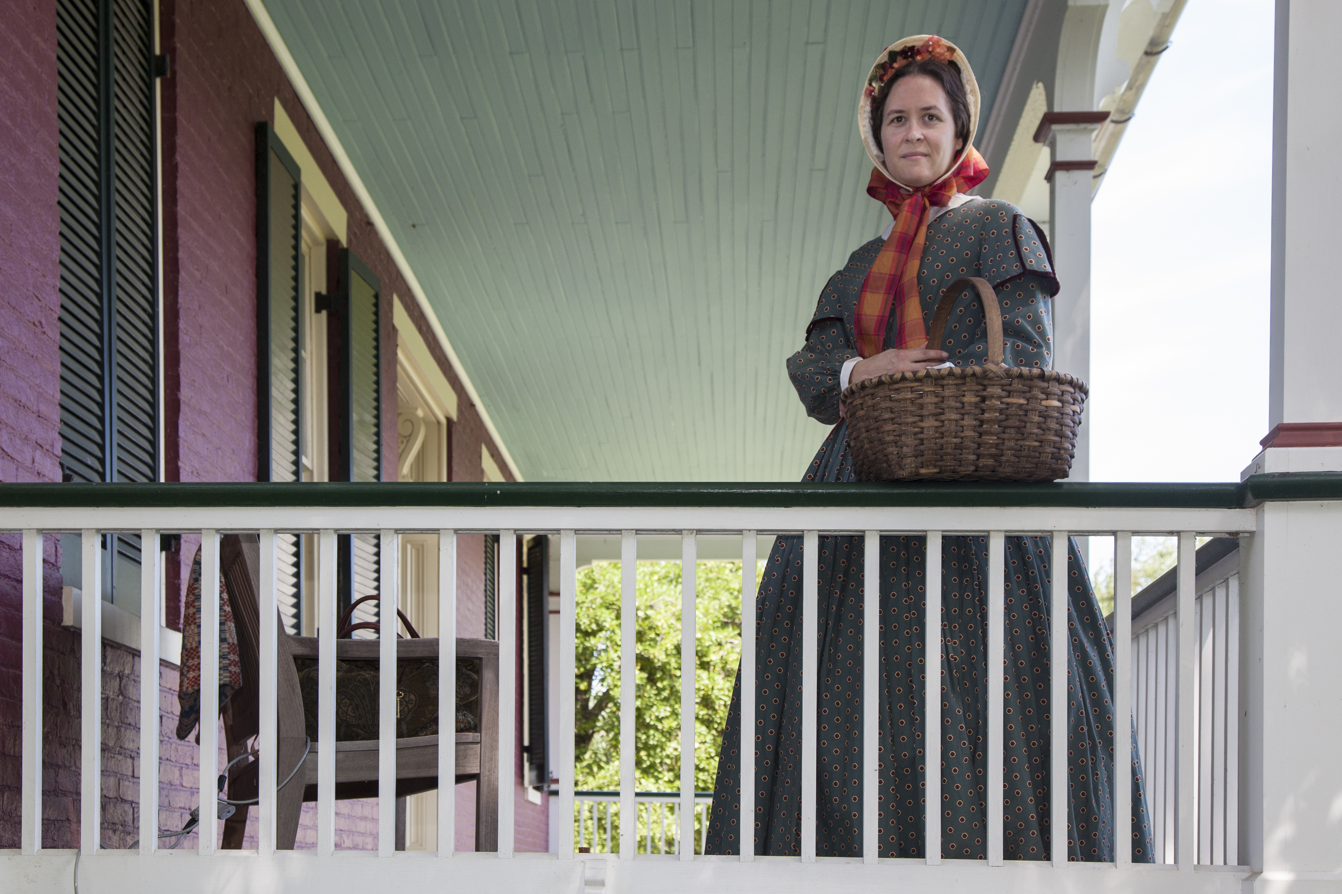 Living historian in 1860s style dress stands on the porch of the Worthington House