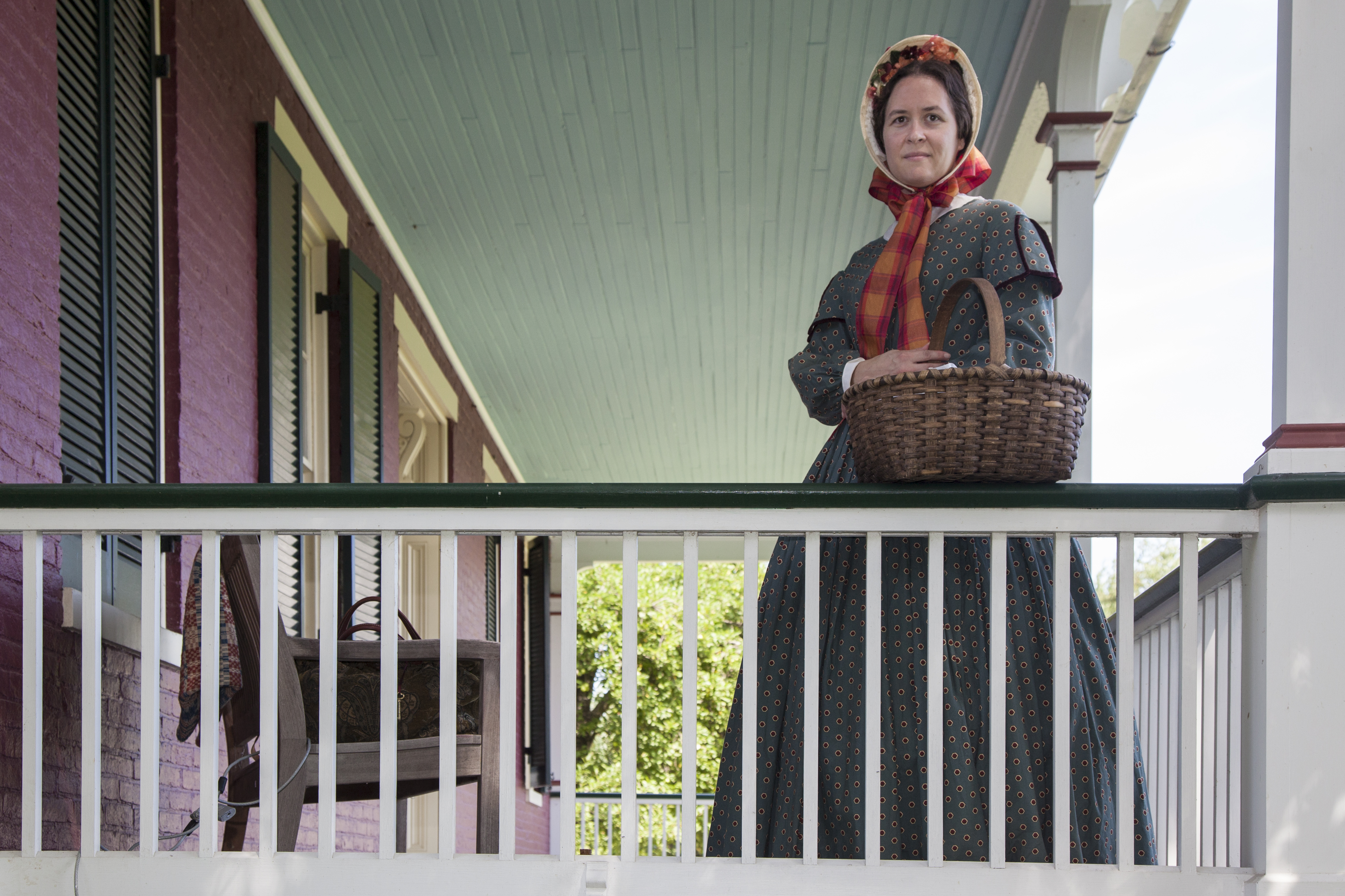 Living historian in 1860s style dress stands on the porch of the Worthington House