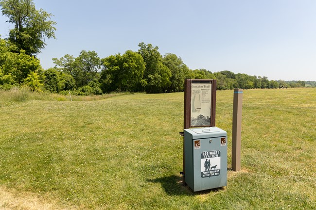 A mowed trail and grass field behind a trailhead sign.
