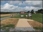 Three wayside stand on the edge of farm fields. A red barn is in the distance.