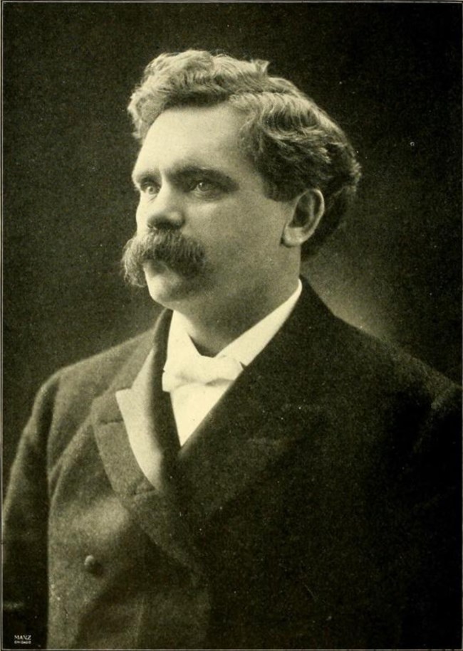 Black and white photo of Brigham Henry Roberts. Young man with light-colored eyes, parted, wavy hair, and thick, drooping mustache; wearing a suit jacket and white shirt.