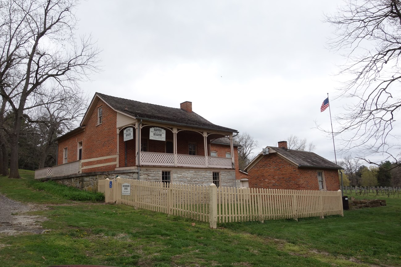 Nauvoo Mormon History Museum a brick building with a pitched roof and a porch on a green, grassy property.