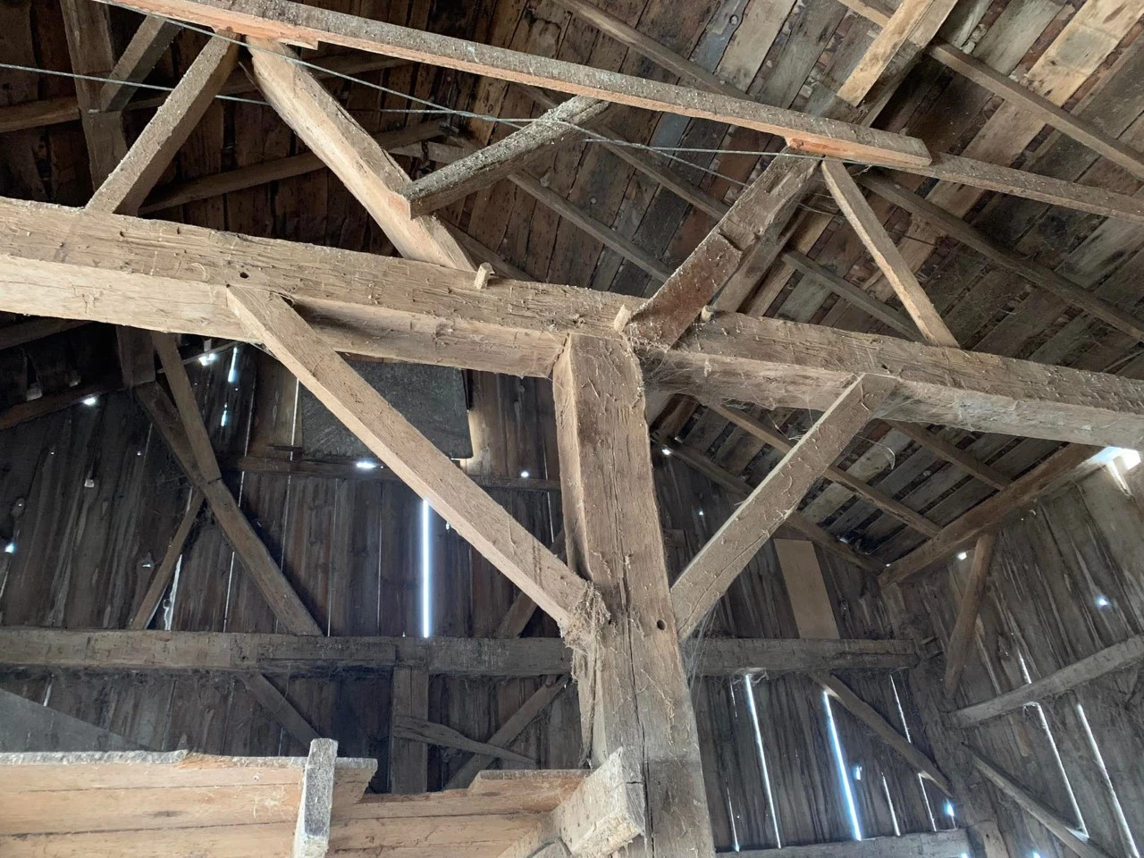 Hand-hewn upright and beams with pegs holding them together. Underside of roof and back wall are visible behind the supporting structures.