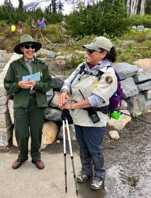 Volunteer and Ranger stand at the base of a trail while having a conversation.