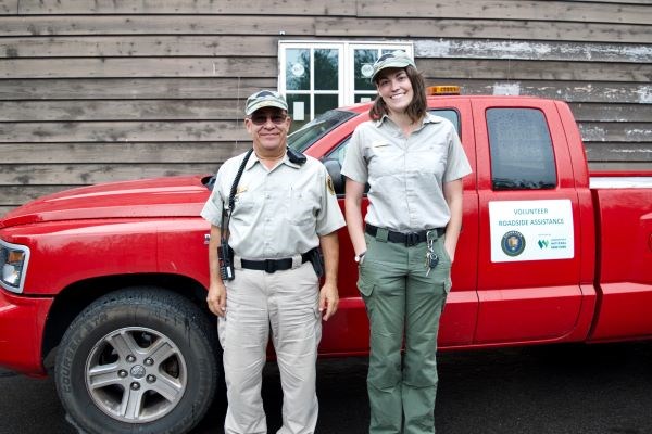 Two volunteers in uniform stand in front of a truck.