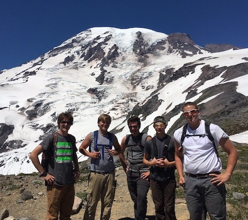 Five young men standing on a trail in front of a glaciated mountain.