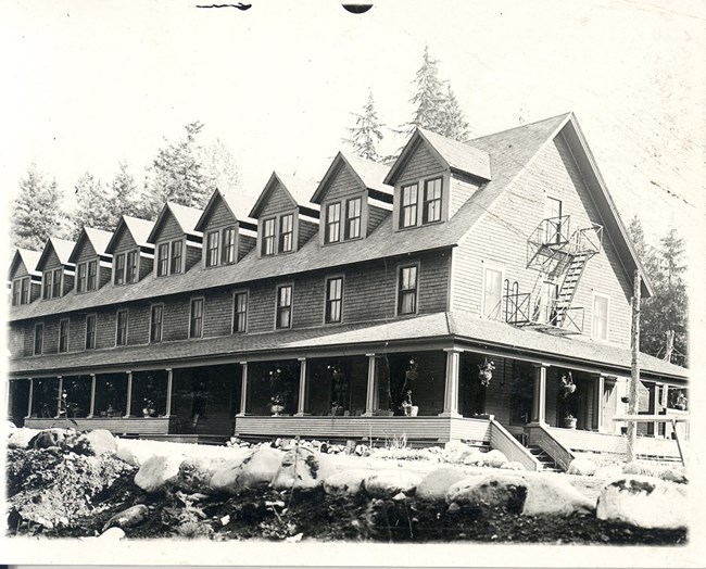The first National Park Inn at Longmire opened in 1906. Black and white image of the north side of the first National Park Inn.