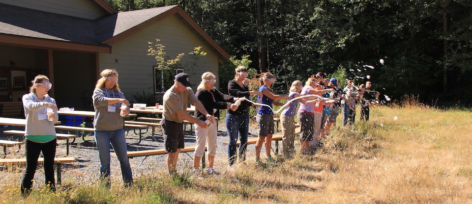 A ring of teachers hold soda bottles spraying plumes of foam.