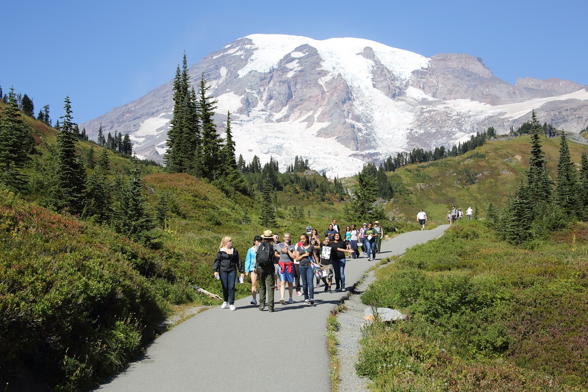 Field Trip A ranger leading a group of students along a paved path with Mount Rainier in the background