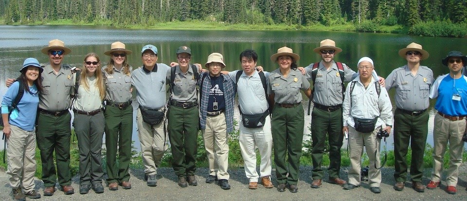 Several people stand in a row with their arms around each other, some Japanese, some dressed as park rangers. Several people stand in a row with their arms around each other, some Japanese, some dressed as park rangers.