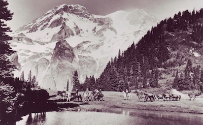 A string of horseback riders circle a subalpine lake with Mount Rainier rising in the background. A string of horseback riders circle a subalpine lake with Mount Rainier rising in the background.