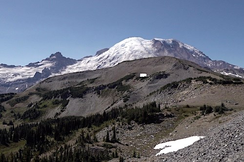 A rounded ridge of grey rock in front of the glaciated peak of Mount Rainier.