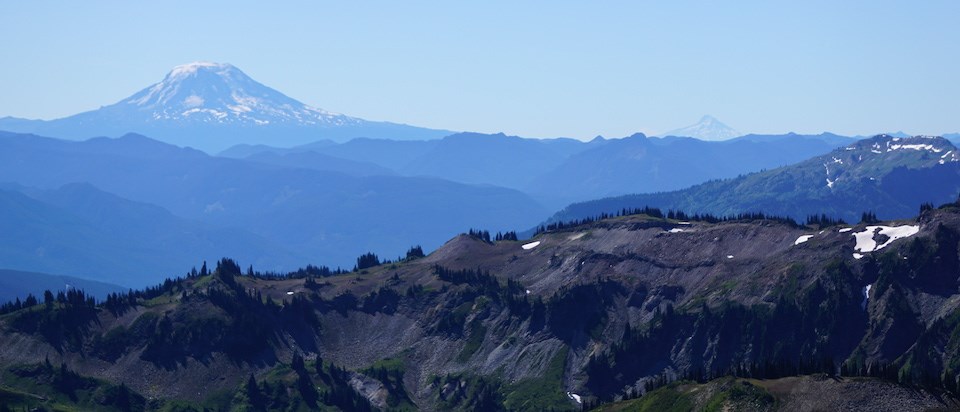 A series of mountain ridges with two distant volcanic peaks rising above them.