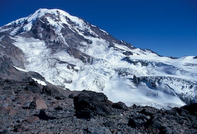 A glacier-filled valley descending from the peak of Mount Rainier, viewed from a rocky ridge.