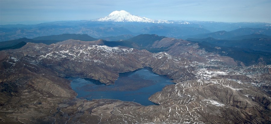 View of a lake surrounded by remains of volcanic debris flows with Mount Rainier in the distance.