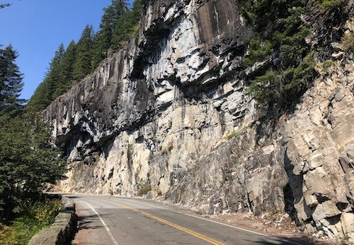 White and tan cliffs hang over a paved road.