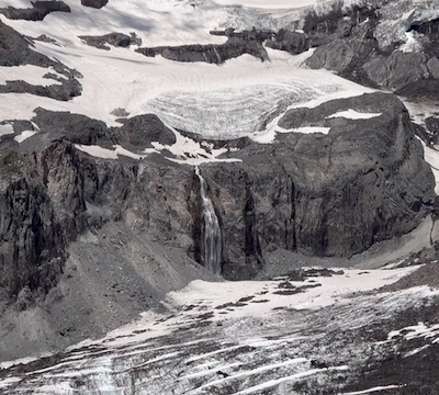 A waterfall emerges from a glacier, falls over a cliff, and merges with another glacier.