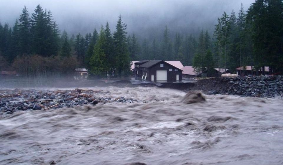 A wide muddy river rages dangerously close to several buildings